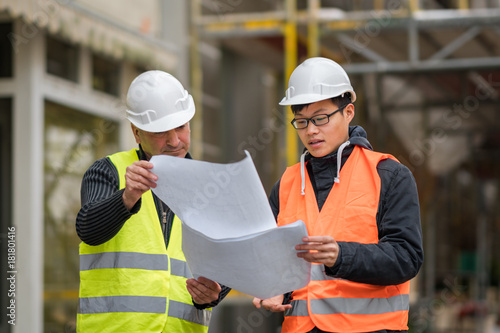 Young Asian apprentice at work on construction site with senior engineer. Outdoors