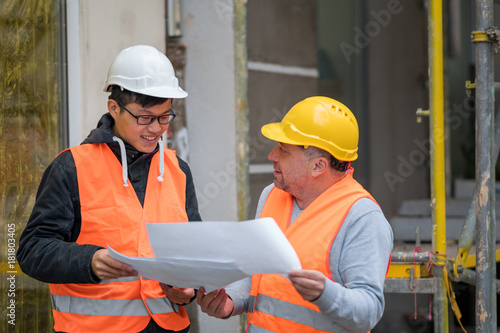 Young Asian trainee engineer at work on construction site with the senior manager. Outdoors