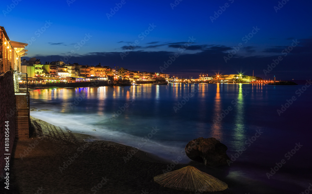 Beautiful evening with night shore with a beach and umbrellas and highlighted with bright colorsin Hersonissos bay Crete, Greece