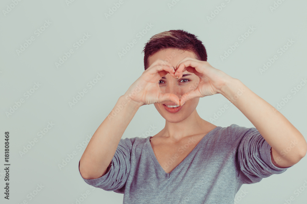 Happy beautiful young woman shows heart shape hands on bright green grey background. Positive human emotions, face expressions, feelings, body language, life perception Happy beautiful young woman shows heart shape hands on bright green grey background. Positive human emotions, face expressions, feelings, body language, life perception