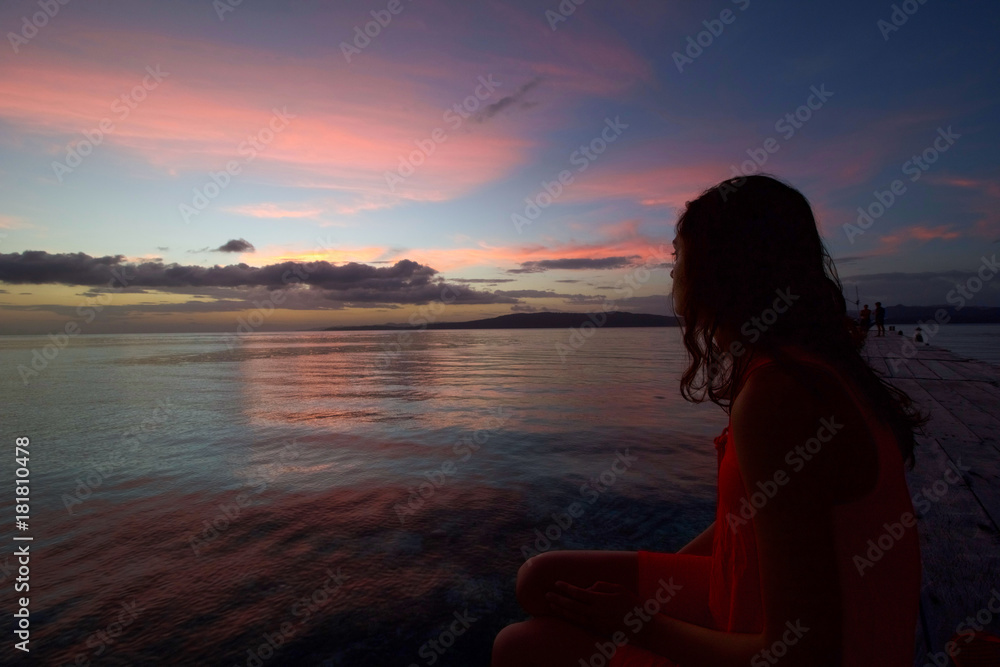 tropical sunset with scenic colors of the sky and young woman sitting and watching