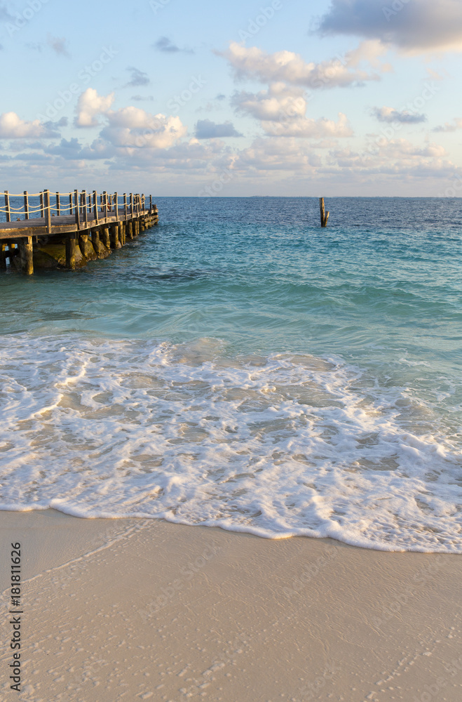 Morning at the Caribbean shore. Long wooden pier on the left. Foamy waves and turquoise water. Peaceful scenery. Wallpaper.