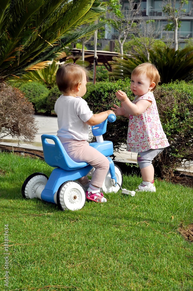two little baby girls on bike in summer park two little baby girls on bike in summer park