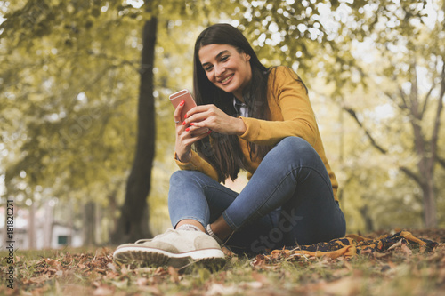 Young woman sitting at nature using phone.