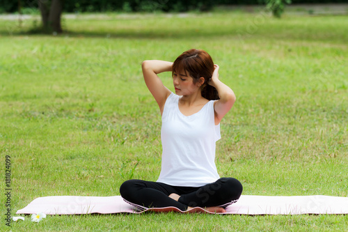 A pretty thai woman sitting on a mat and gathering her hair to practice yoga in park.