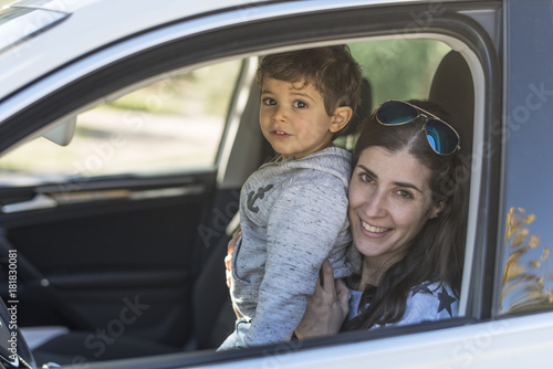 Mother and baby son posing in portrait image inside her car and looking at camera while smiling