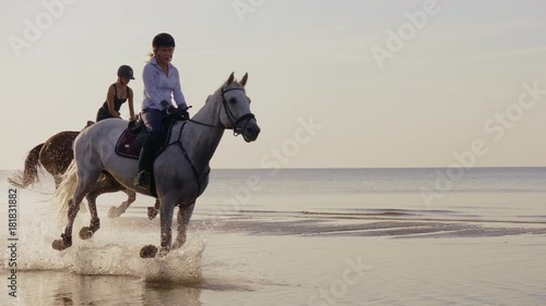 Two women riding horses on a beach
