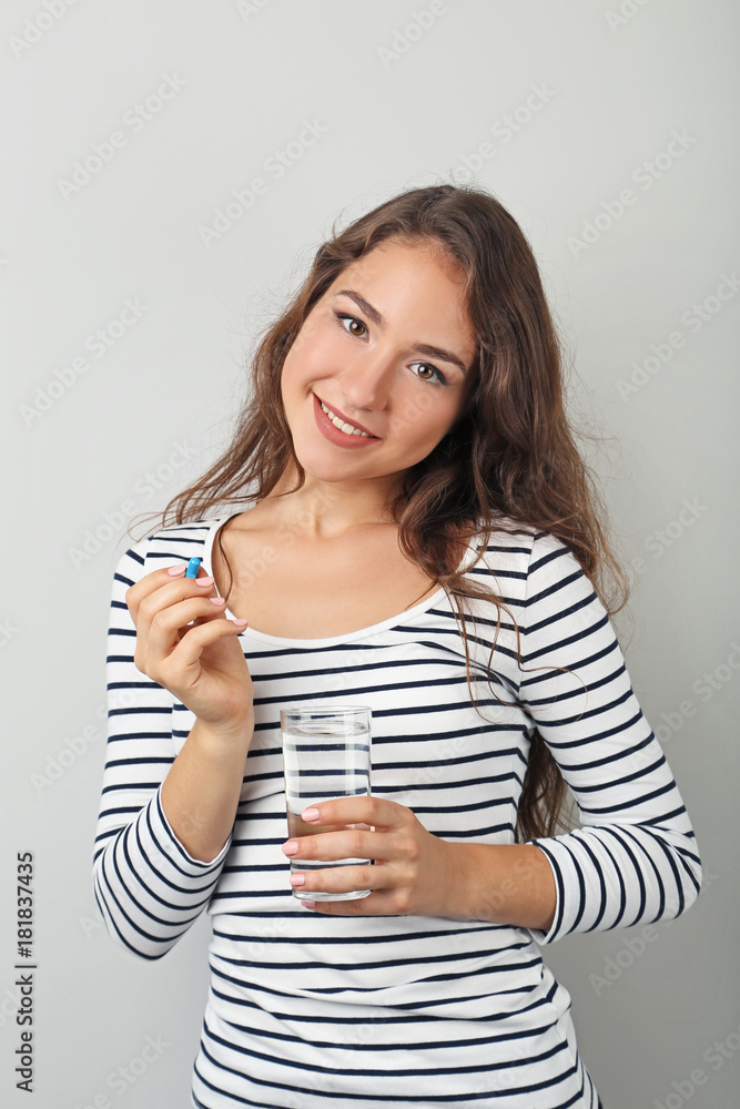 Portrait of young woman with pill and glass of water on grey background Portrait of young woman with pill and glass of water on grey background