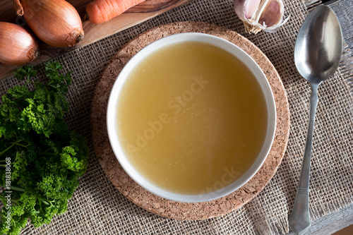 Chicken bone broth with vegetables in the background, top view photo