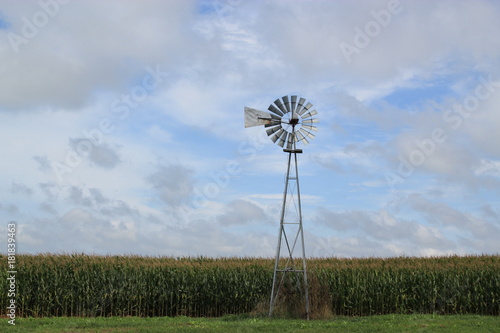 old fashioned windmill in corn field with cloudy blue sky