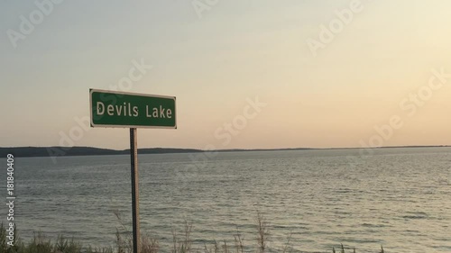 Devils lake sign at sunset with lake water in background; shot at Devils Lake, ND in July.