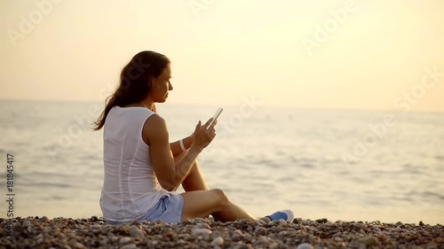 Attractive woman sits on the beach with a cell photo