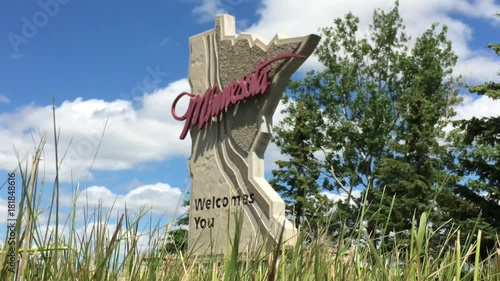 State of Minnesota welcomes you sign shot from ground level, angled and with blue sky and clouds in background.   
