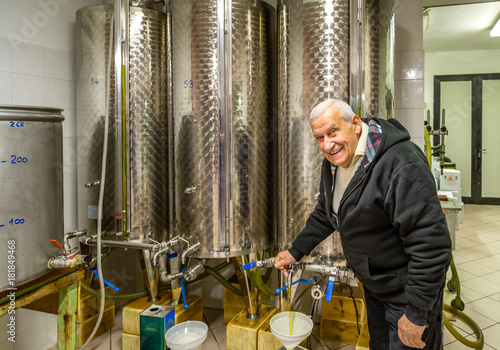 Obraz w ramie old man opens tap of storage silo of olive oil