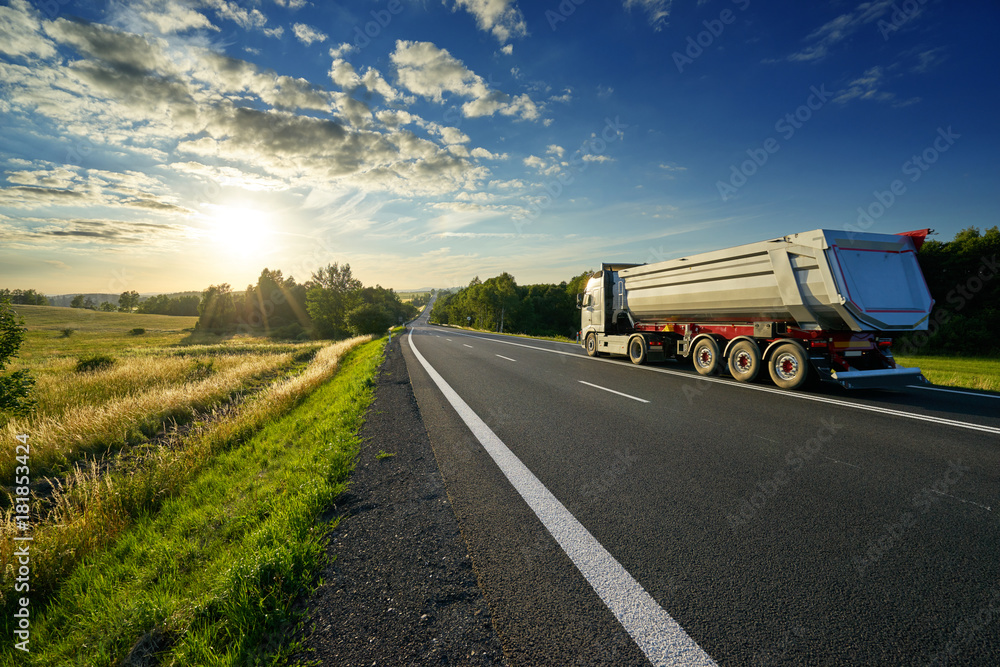 Tipping lorry driving on the asphalt road in the rural landscape at sunset Tipping lorry driving on the asphalt road in the rural landscape at sunset