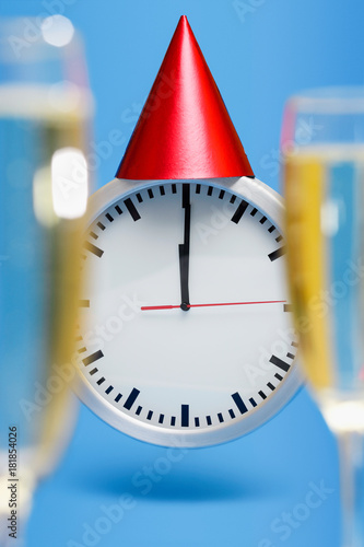 series of a Cute simple clock wearing a Red Party Hat on New Years Eve at Midnight, on bright blue background and two blurred champagne glasses