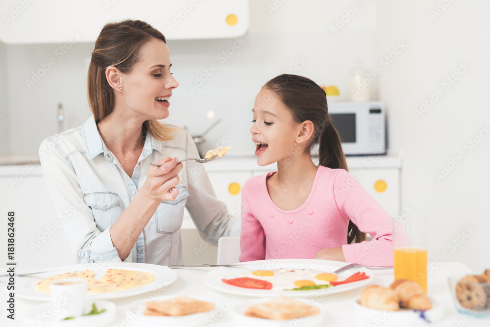 Mom and daughter are sitting in the kitchen and having breakfast. They have fun at breakfast. Mom and daughter are sitting in the kitchen and having breakfast. They have fun at breakfast.