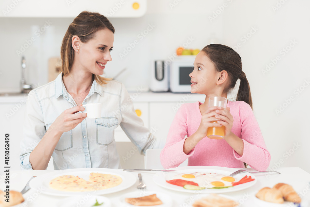 Mom and daughter are sitting in the kitchen and having breakfast. They have fun at breakfast.