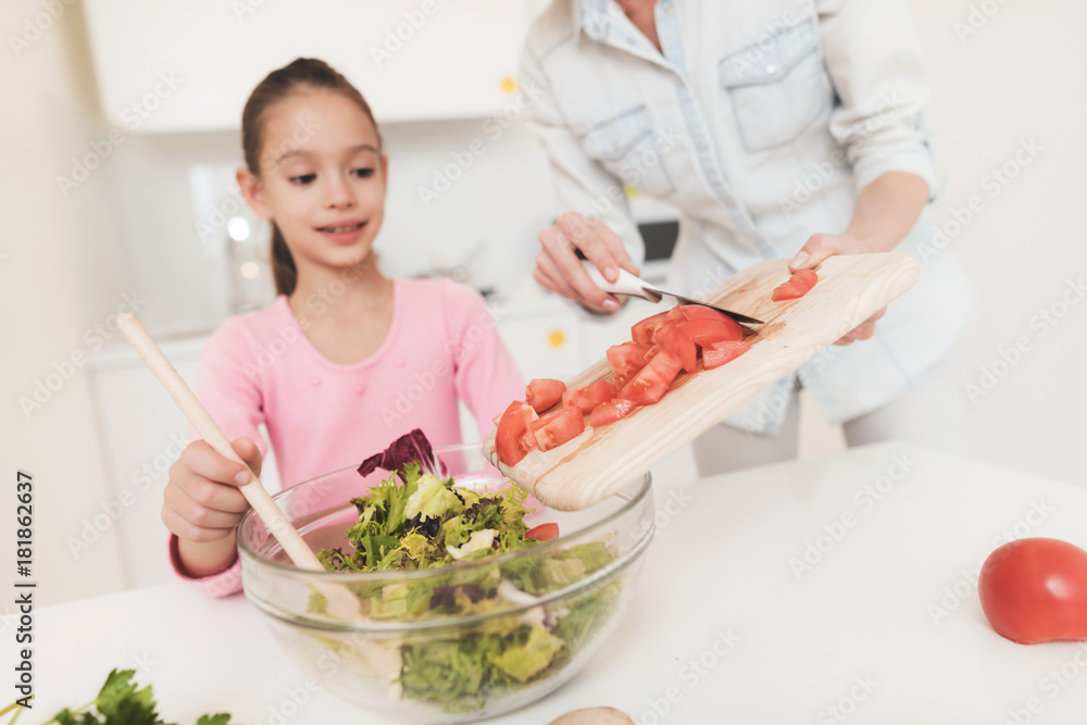 The girl is learning to prepare a salad in a light kitchen.