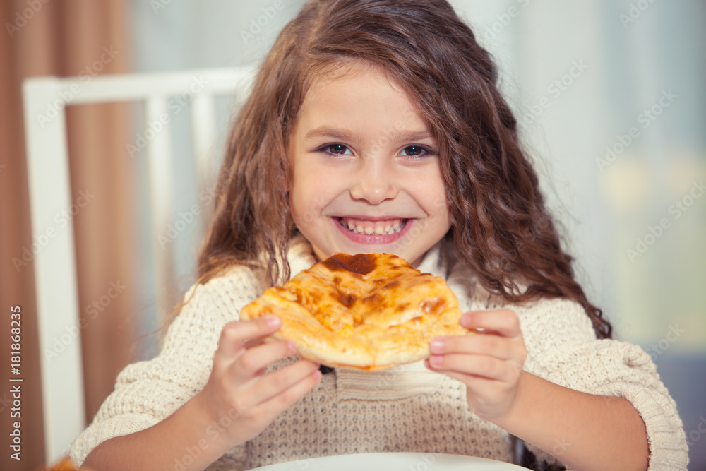 A girl in a white jacket is eating pizza at home, smiling, cake