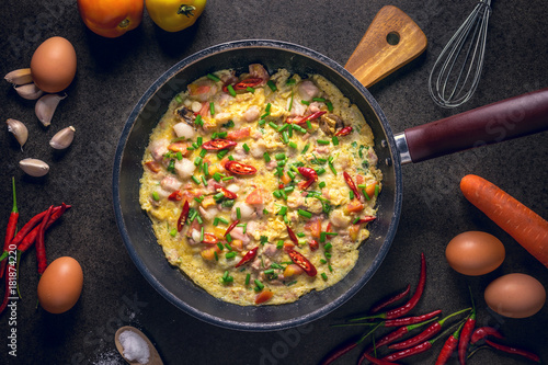 Omelette in frying pan on dark background, top view. garlic and fresh tomatoes. Traditional