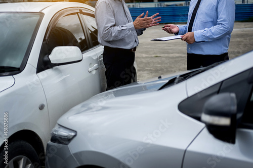 Insurance agent writing on clipboard while examining car after accident claim being assessed and processed.