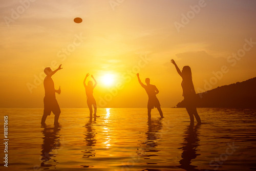 Silhouette image of young people playing on the beach in summer sunset