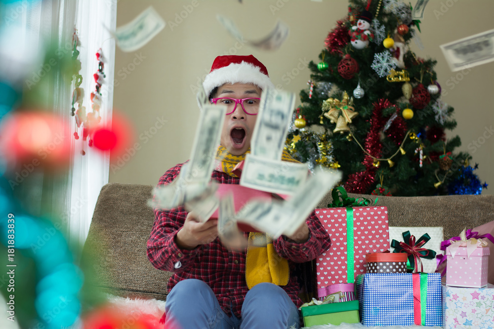 Young man is surprised with gift box and money while open christmas gift box at home.