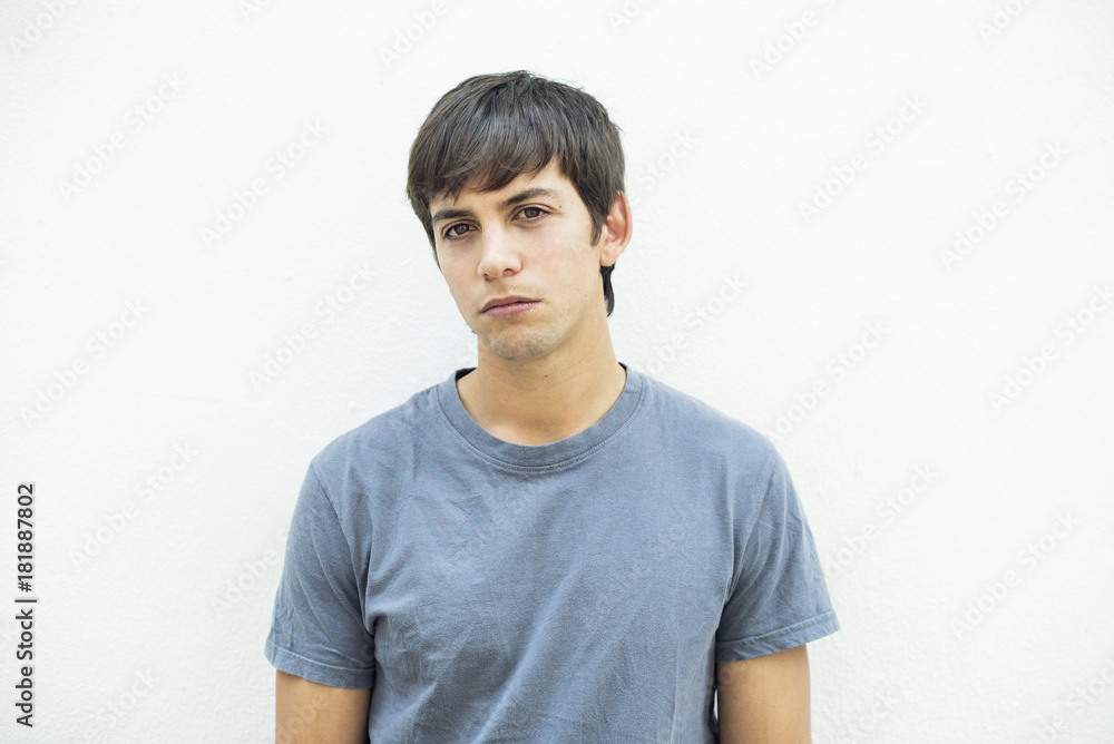 Retrato frontal de hombre con cabello castaño y camiseta gris sobre fondo blanco con expresión de pena, tristeza. Retrato frontal de hombre con cabello castaño y camiseta gris sobre fondo blanco con expresión de pena, tristeza.