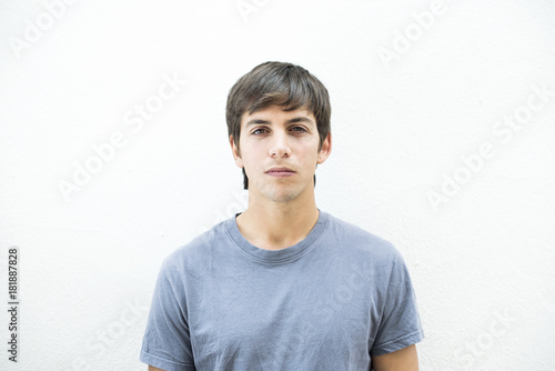 Retrato frontal de hombre con cabello castaño y camiseta gris sobre fondo blanco con expresión seria. photo
