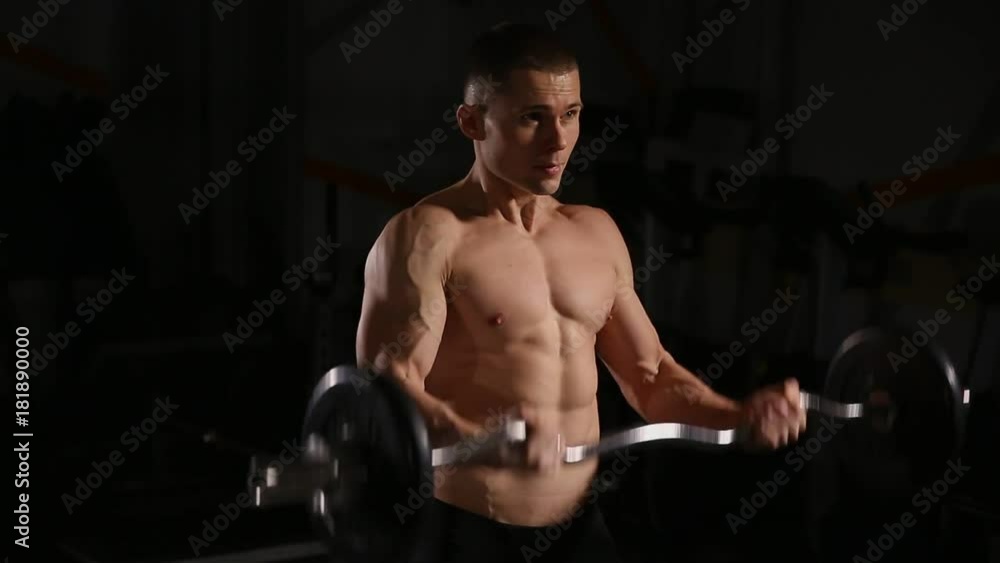 Handsome man with big muscles, posing in the gym muscular man lifting weights over dark background muscular man working out in gym doing exercises with barbell at biceps strong male. close-up Handsome man with big muscles, posing in the gym muscular man lifting weights over dark background muscular man working out in gym doing exercises with barbell at biceps strong male. close-up