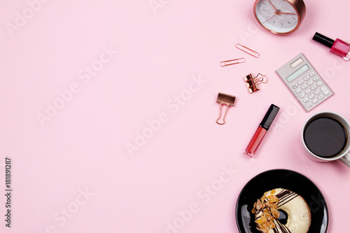 Flat lay home office desk workspace with coffee and donut, pen, notepad, calculator, paperclip and lipstick on pink background. Top view.