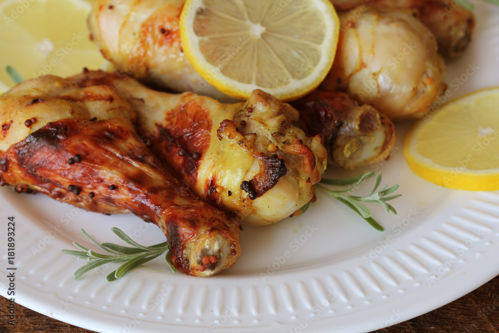 Grilled chicken legs with mustard on wooden table served on white plate with rosemary. BBQ dinner background