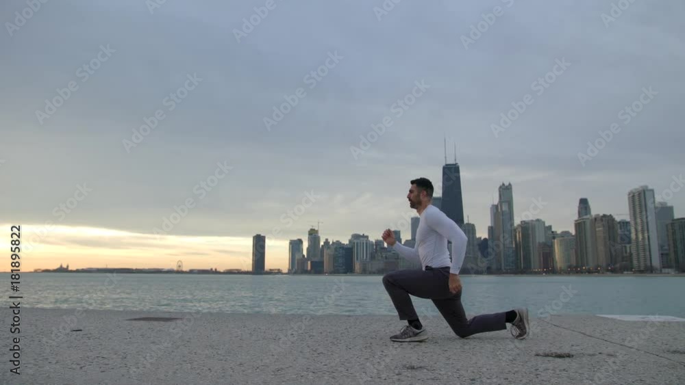 Man is stretching legs on ebankment. Athlete training outdoors. Downtown with skyscrapers on the background. Sunrise. Man is stretching legs on ebankment. Athlete training outdoors. Downtown with skyscrapers on the background. Sunrise.