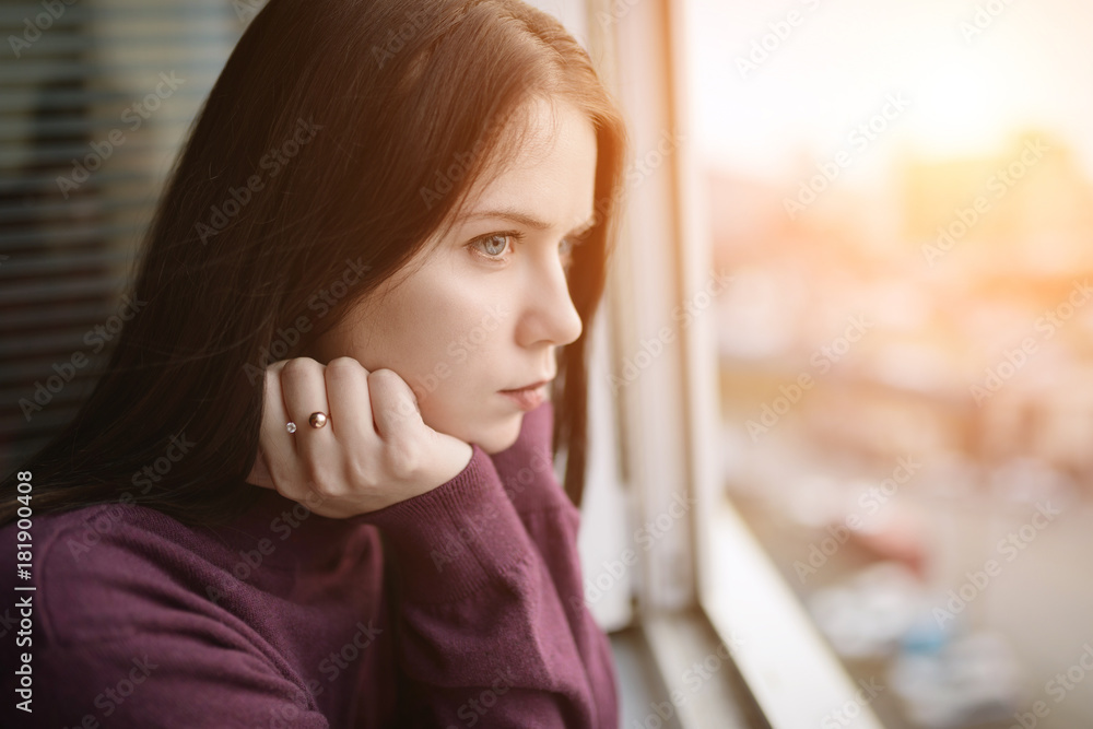Sad woman looking through the window at sunset. Sad woman looking through the window at sunset.