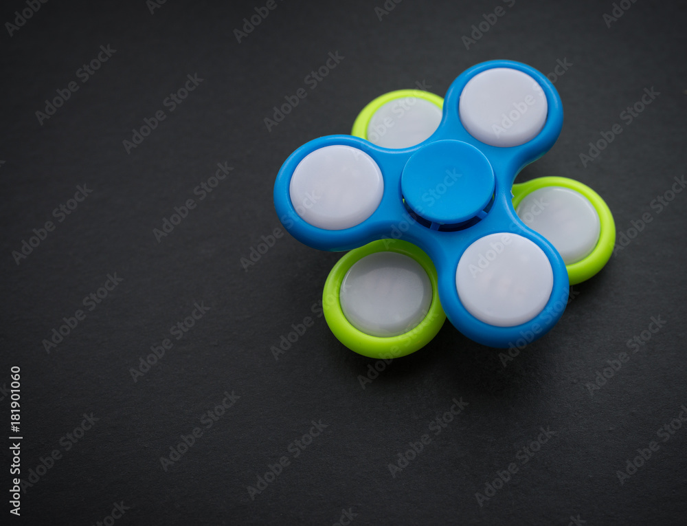 Fidget spinner - anxiety relief toy on dark background. Selective focus. Fidget spinner - anxiety relief toy on dark background. Selective focus.
