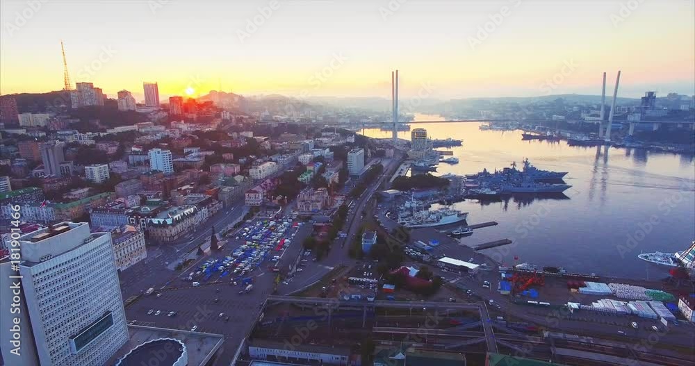 Flying above Vladivostok city center, great aerial view of Golden Horn harbour with moored ships, and Golden Bridge. Early morning, beautiful sunrise. Russia Flying above Vladivostok city center, great aerial view of Golden Horn harbour with moored ships, and Golden Bridge. Early morning, beautiful sunrise. Russia