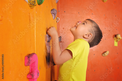 Adorable little boy climbing on wall in gym