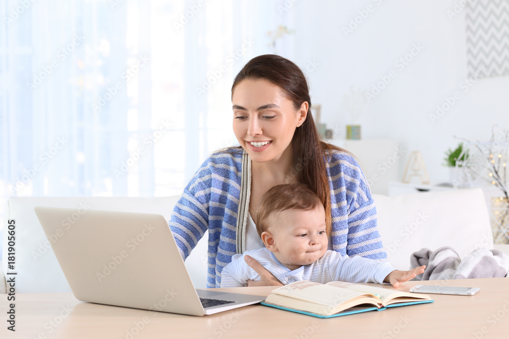 Young mother holding baby while working in home office Young mother holding baby while working in home office