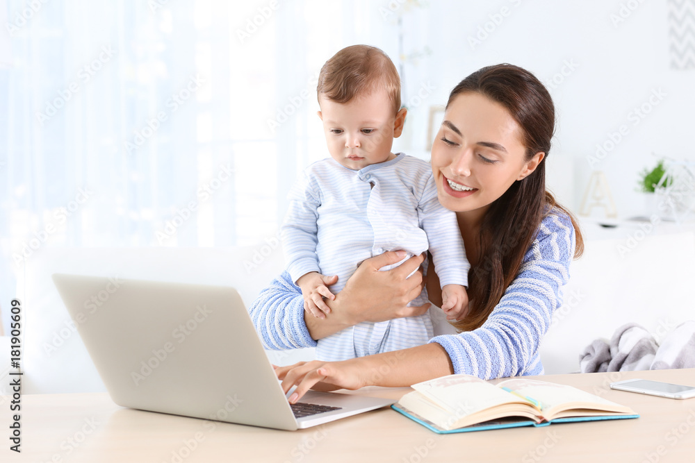 Young mother holding baby while working in home office Young mother holding baby while working in home office