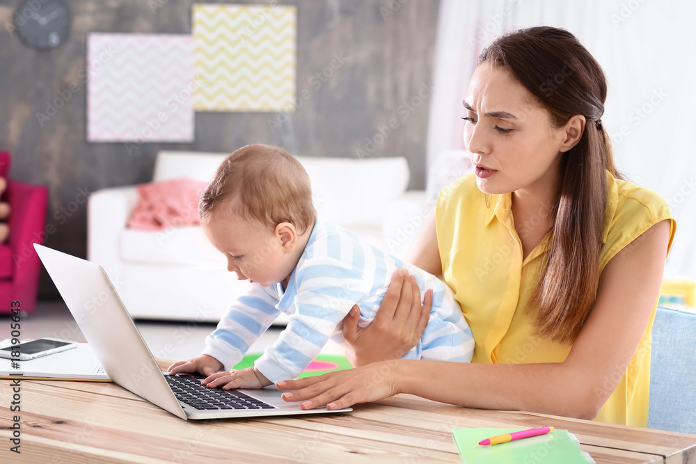 Young mother holding baby while working in home office Young mother holding baby while working in home office