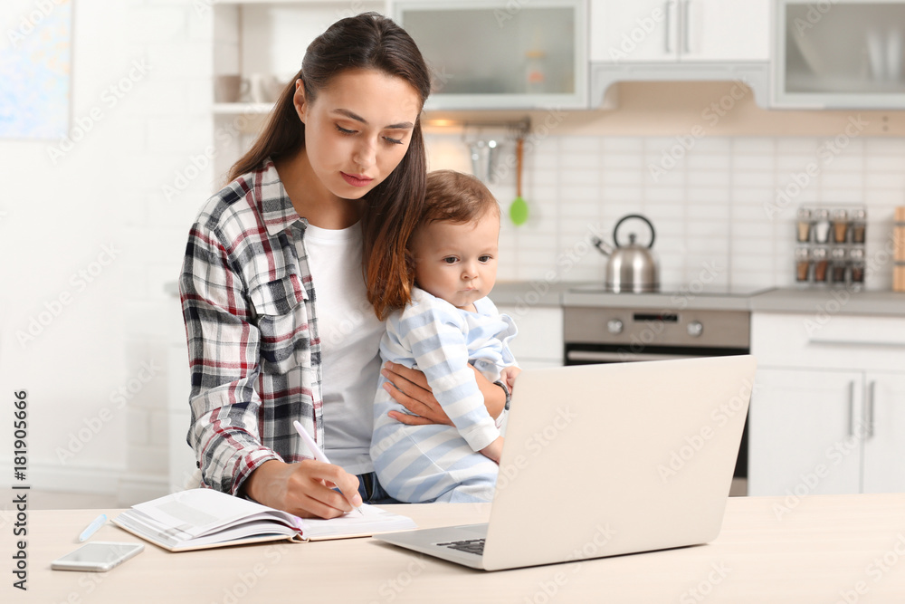 Young mother holding baby while working in home office Young mother holding baby while working in home office
