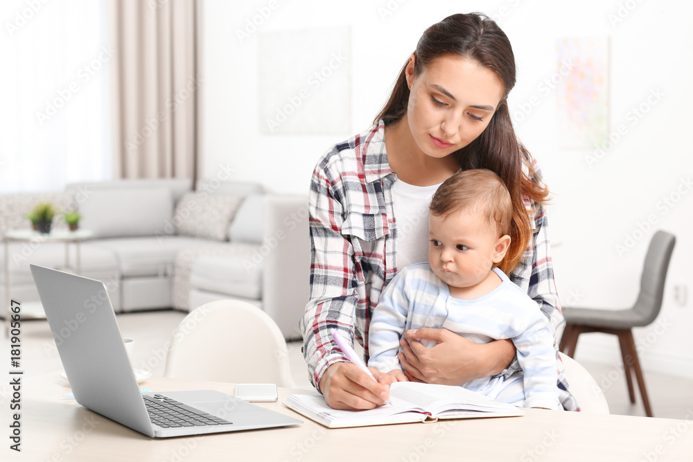 Young mother holding baby while working in home office Young mother holding baby while working in home office