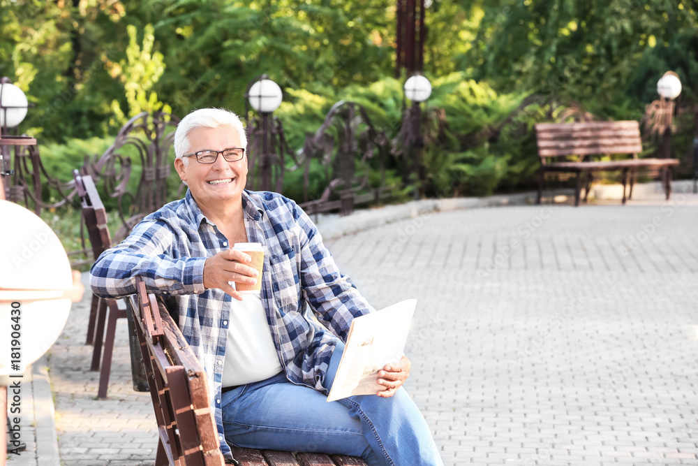 Fototapeta premium Handsome mature man with coffee and newspaper in park
