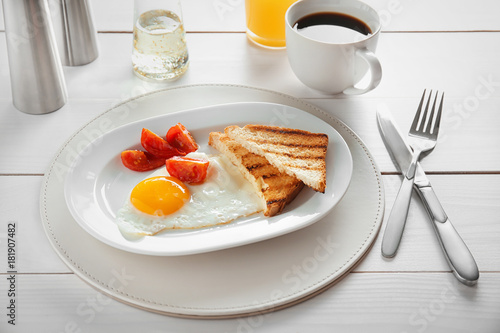 Plate with fried egg, toasts and tomatoes on table