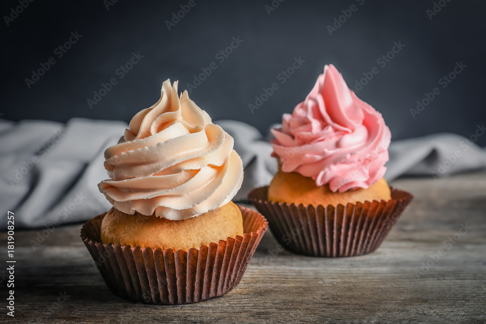 Yummy cupcakes on wooden table against dark background