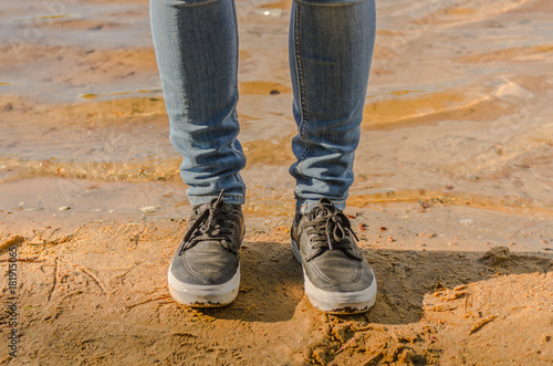 Female legs in jeans and sneakers on the beach