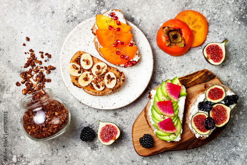 Healthy breakfast toasts with avocado, peanut butter, banana, chocolate granola, cream cheese, figs, blackberry, persimmon, pomegranate, chia seeds. Top view, overhead