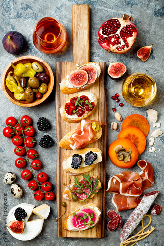 Appetizers table with italian antipasti snacks and wine in glasses. Brushetta or authentic traditional spanish tapas set, cheese variety board over grey concrete background. Top view, flat lay