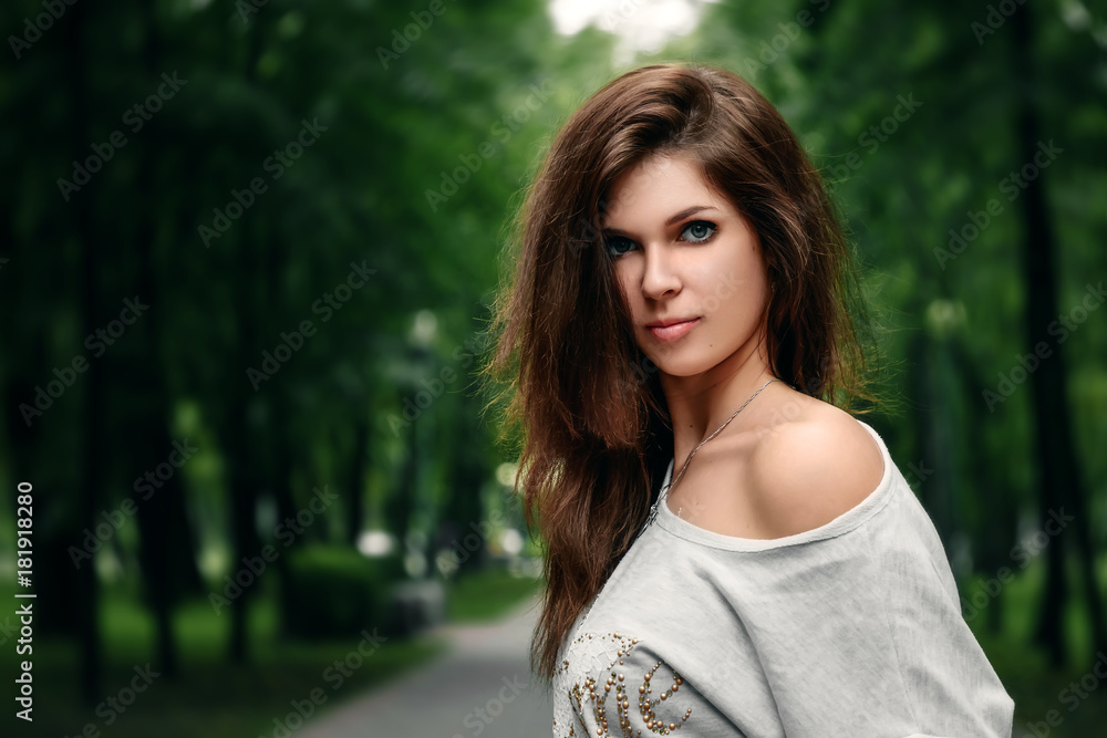Naklejka premium Beautiful young brown-haired girl in the park on a warm summer day